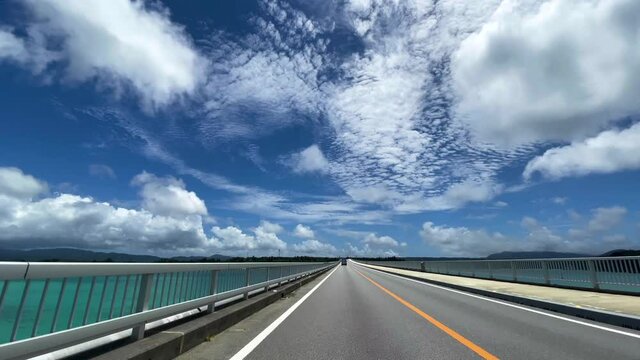 OKINAWA, JAPAN - JUNE 2021 : Driving at Kouri Island bridge. Wide camera point of view (POV), seaside road driving shot. Blue sunny summer sky.