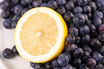 a sliced lemon wedge resting on a pile of blueberries on a white dish