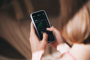 Stock market investor young woman holding a phone investment app index growth chart
