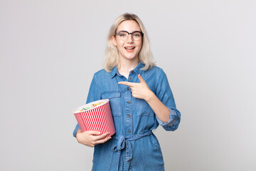 young pretty albino woman looking excited and surprised pointing to the side with a pop corns bucket