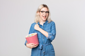 young pretty albino woman feeling happy and facing a challenge or celebrating with a pop corns bucket