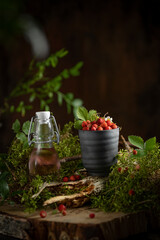Wild strawberries in a cup in the wood with green leaves and plants around, beautiful dark mood rainy studio image with forest concept, healthy organic berries, copy space. 