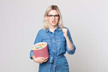 young pretty albino woman shouting aggressively with an angry expression with a pop corns bucket