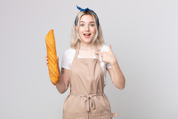 young pretty albino woman feeling happy and pointing to self with an excited with a bread baguette