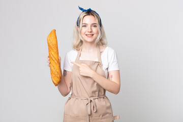 young pretty albino woman smiling cheerfully, feeling happy and pointing to the side with a bread...