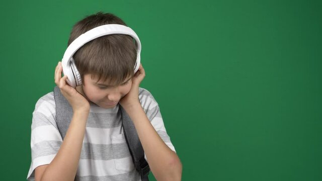 Teenage boy with headphones listening music and nods his head on green screen choma key background