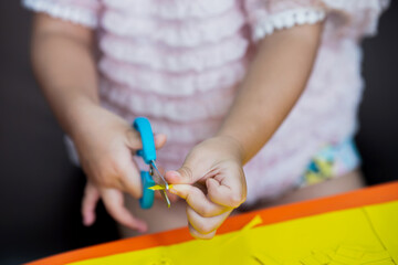 Closeup shot of a child's hand using blue scissors to carefully cut a small piece of yellow colored paper.