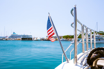 The flag of the United States flutters in the wind on a stainless steel flagpole at the stern of a motor yacht. Marina in the port city in beautiful summer sunny weather.