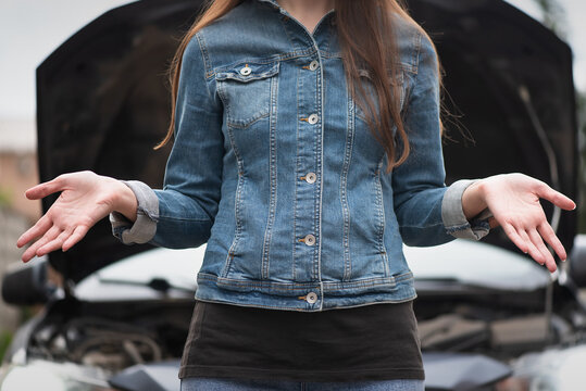 A woman is spreading her hands on the broken car with open hood background.