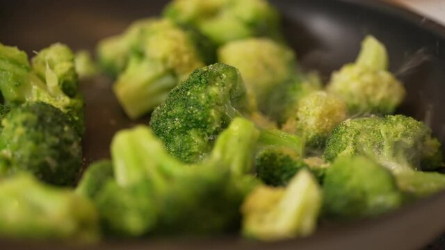 Skillet full of freshly cut broccoli cooking on the stove top - slow motion