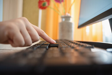 Woman is pressing a key on the computer keyboard by her index finger close up.