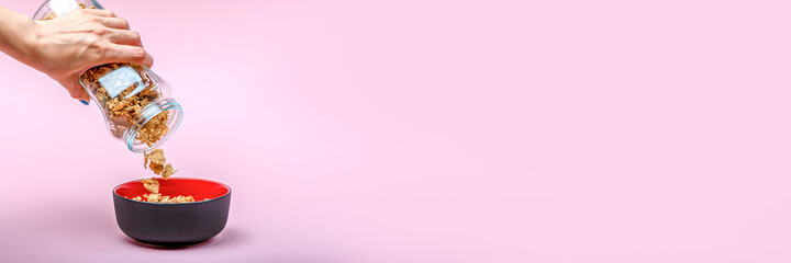 Muesli on a pink background. Pour dry muesli flakes by hand into a bowl. Pouring muesli from a...