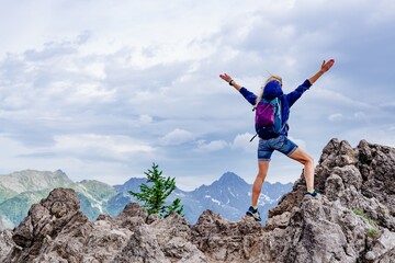 Blonde woman tourist standing on a rock with his arms spread wide looking in the distance.