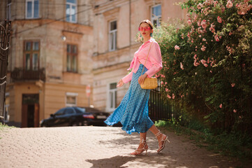 Summer street fashion conception: elegant woman wearing trendy pink sunglasses, shirt with knot,...