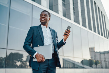 Joyful black businessman with laptop and smart phone