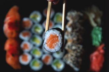 A girl holds a small roll with chopsticks on the background of a set with rolls