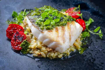 Modern style traditional fried skrei cod fish filet with mushroom rice risotto and oregano salsa relish served as close-up on a Nordic design plate - obrazy, fototapety, plakaty