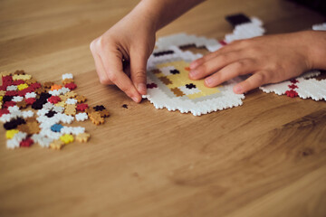 Child making the astronaut made of plastic puzzle tiles over the wooden table. Children's creative...