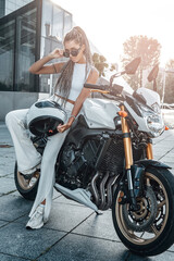 Plakat Woman with motorcycle helmet leaning motorbike on sidewalk