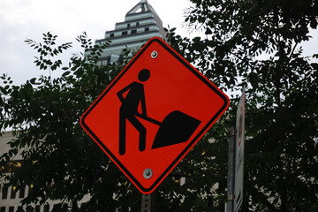 Montreal, QC, Canada - 7-15-2021: A sign of roadwork in downtown with a blurred background of a skyscraper and trees.