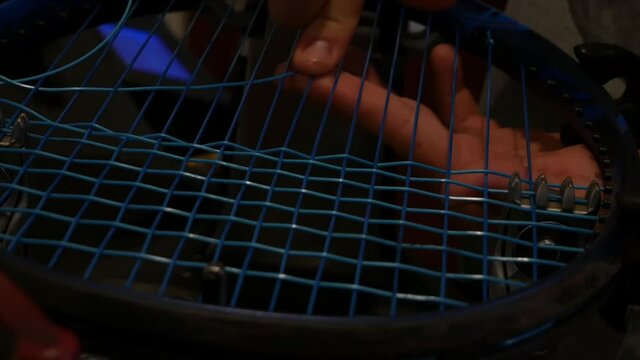 man's hands finely weave tennis racket string