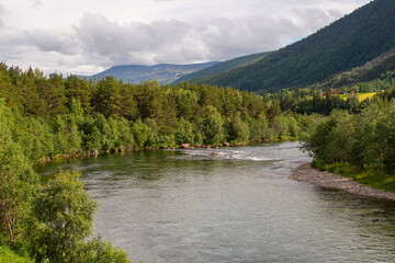 River Glomma in Gudbrandsdalen valley, Norway. Hills, forest and grey, clouded sky. Horizontal.