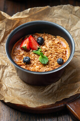 Homemade creme brulee with strawberries and mint in a metal bowl on parchment on a dark brown wooden table