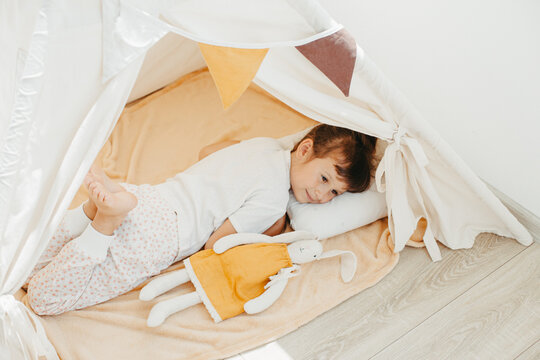 Six years cute girl playing in teepee with fabric tilda bunny at home