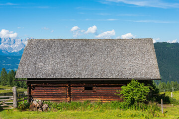 A wooden alpine shed against the backdrop of high alpine mountains. Blurred, weathered wooden shingles, faded from sun, rain and snow. Wooden texture in shades of gray and orange.