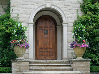 Elegant wood grain front door of stone house in round vestibule, surrounded by vines and flowers