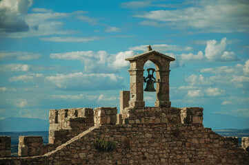 Bell on top of thick stone wall with crenels and merlons at the Castle of Trujillo. A small medieval town in Spain.