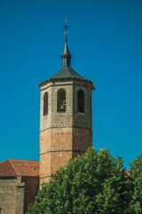 Church bell tower made of bricks and green trees with blue sky, in a sunny day at Avila. A cute city with medieval buildings in Spain.