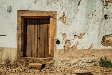 Old house with worn plaster wall and wooden door in cobblestone alley, on sunny day at Marvao. An amazing medieval fortified village in Portugal.