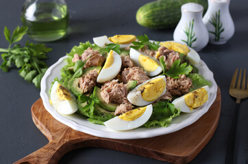 Healthy salad with avocado, tuna, eggs and cucumbers on a white plate on a wooden board