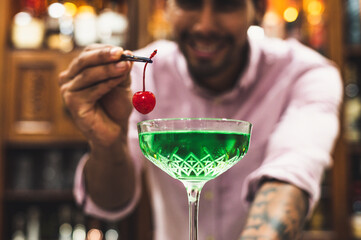 Young barman placing a cherry in a green cocktail, night party concept