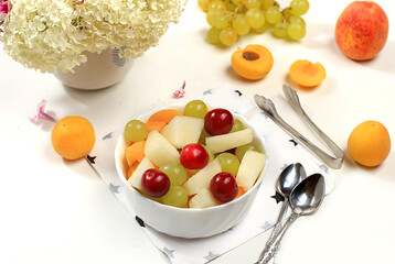 Fruit salad with peach and melon, fresh tropical fruits and berries on a bright sunny table,...