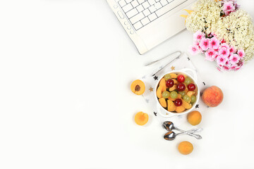 Modern woman's work desk, home office, fruit salad with muesli, grapes, cherries and peaches on a light table. Healthy breakfast with ingredients, healthy lifestyle concept, flat lay