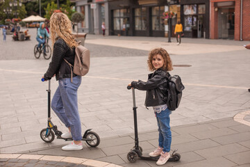 The stylish young mom and daughter are riding scooters