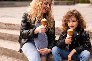 The happy mom and daughter are holding ice cream while walking