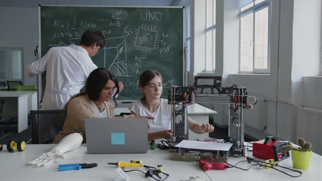 Girls sits on the chairs and learns the work of 3D printer