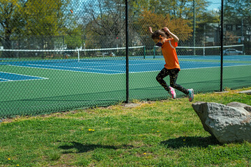 little girl in soccer uniform jumping from rock