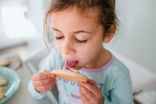 Little girl licking frosting off Easter egg cookie