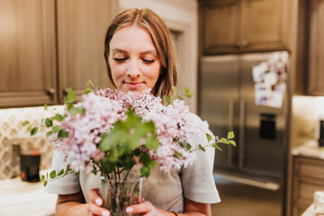 Smiling woman smells fresh cut lilacs in her kitchen