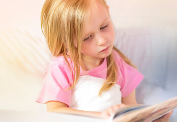 A little girl reads a book before bed in her bed