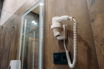 Hotel hand held hair dryer on dark wall. There is a mirror in the background.