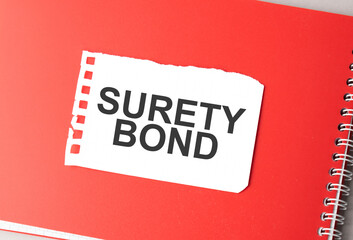 The word Surety Bond on torn paper on red notepad,.