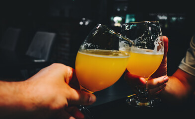 Closeup view of a two glass of beer in hand. Beer glasses clinking in bar or pub