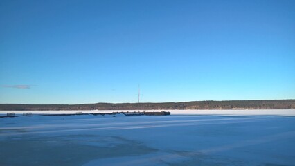 View of frozen lake and concrete pier in winter under blue sky
