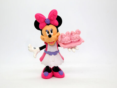 Minnie Mouse. Toy. Cartoon characters from Walt Disney Pictures Studios. Minnie is Mickey Mouse's girlfriend. Pink and white dress. Doll with interchangeable clothes. Minnie with a cake in hand.