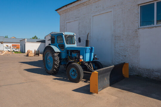 An old blue tractor stands on the asphalt near the warehouses.